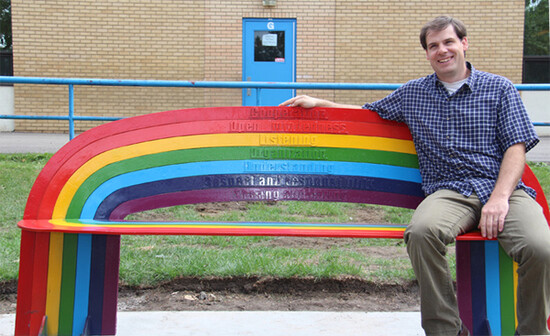 man sitting on bench shaped and coloured like a rainbow